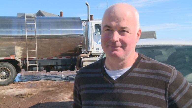 Man in sweater in front of dairy truck.