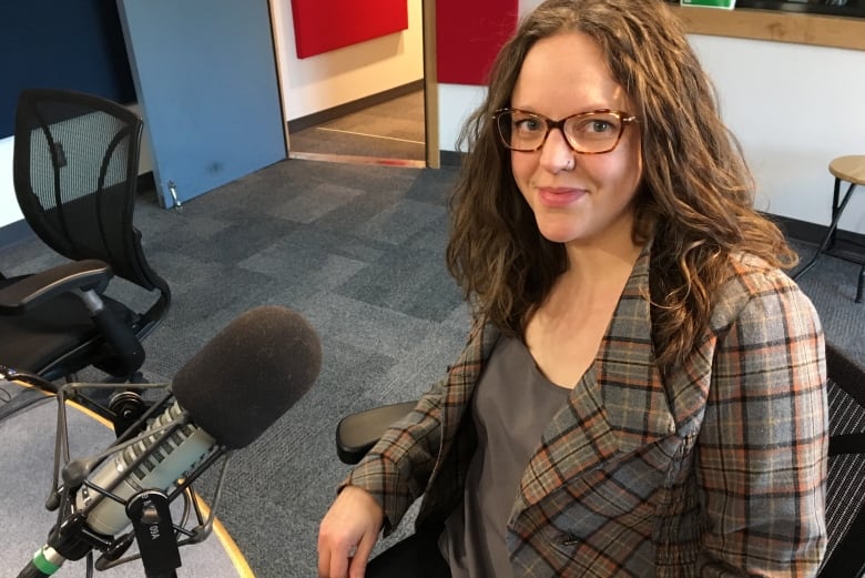 Woman with brown curly hair and red glasses sitting at a desk with a microphone.