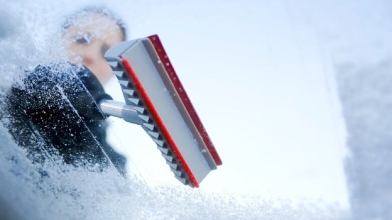 View from inside a vehicle where someone scrapes off ice from the window