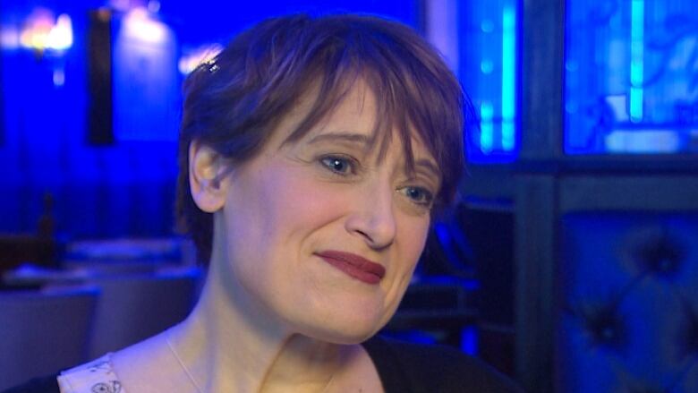 A woman smiles in front of a backdrop lit blue