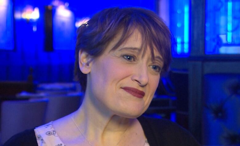 A woman smiles in front of a backdrop lit blue