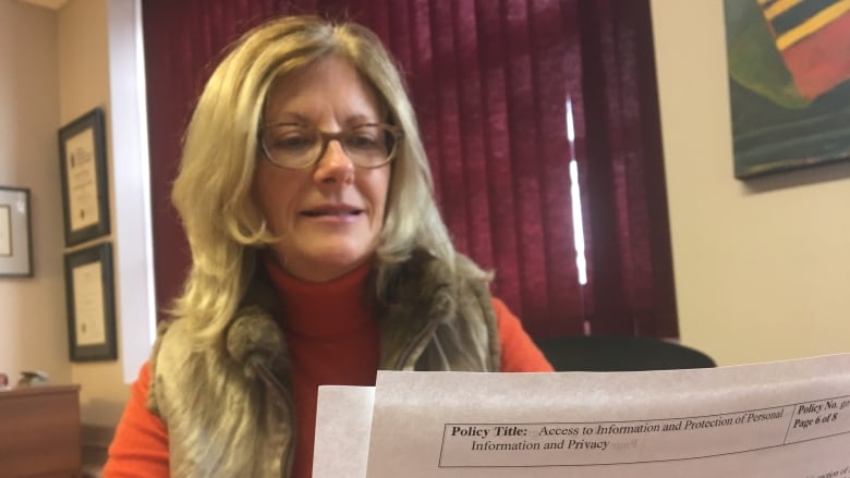 Blonde woman in glasses looks at document. 