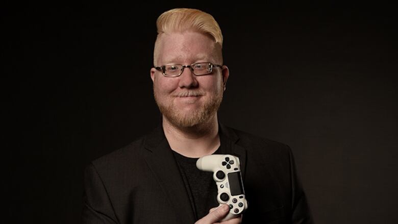 A man poses in front of a black backdrop holding a videogame controller.