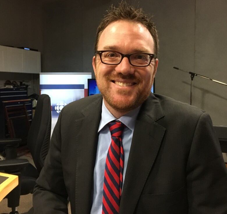 A smiling man wearing a suit, with glasses and a beard.