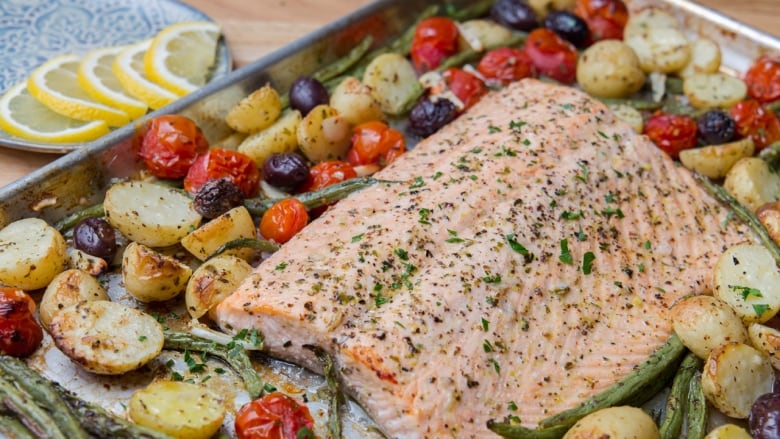 A large piece of baked salmon surrounded by potatoes, green beans and cherry tomatoes on a baking sheet. 