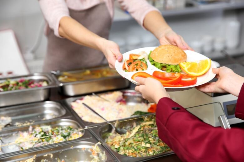 A cafeteria worker hands a plate filled with food to a person.