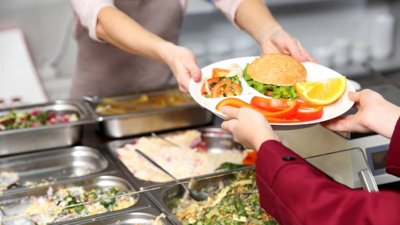 A cafeteria worker hands a plate filled with food to a person.