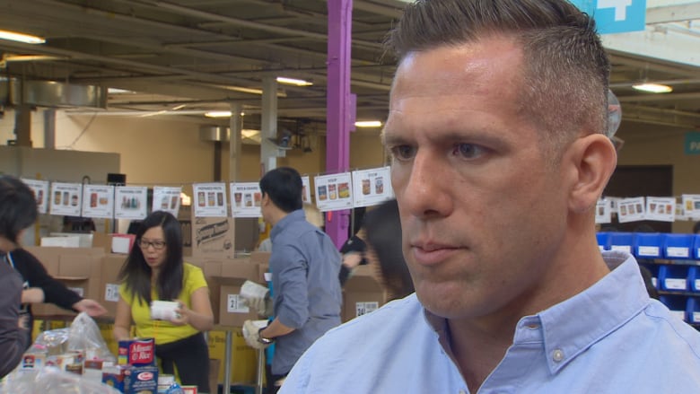 A man standing near volunteers who are packing food hamper donations.