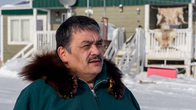 A man wearing a parka stands outdoors in winter.