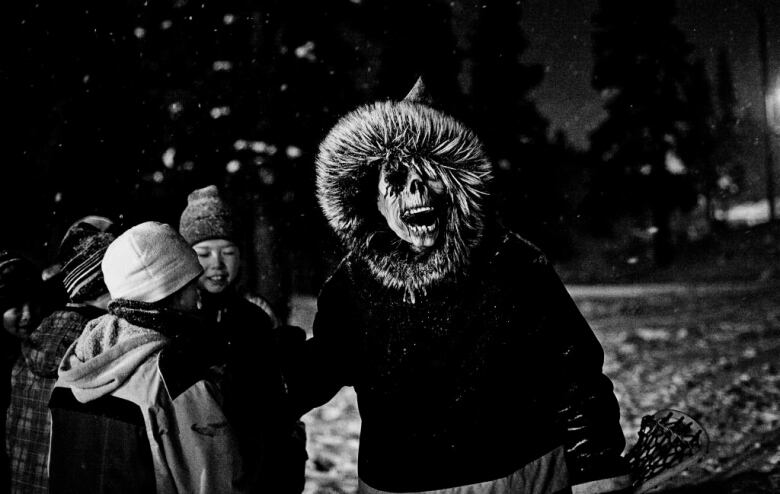 A person in a skull mask and parka confronts three children.