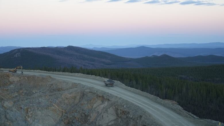 An ore truck is seen from above, driving on a remote road with mountains in the background.