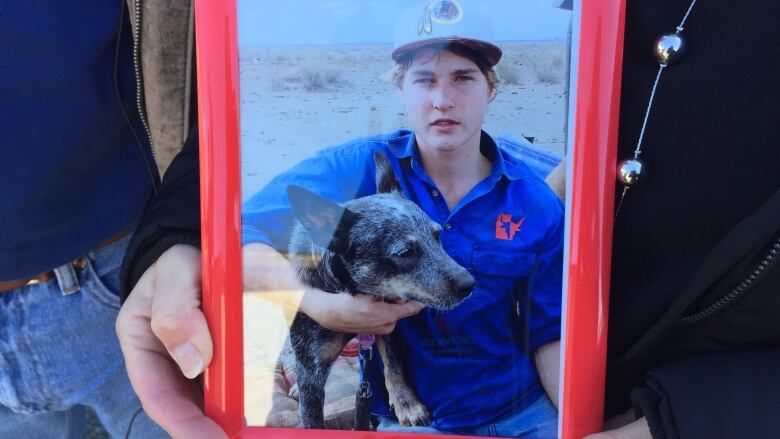 A hand hold a framed photograph of a young boy with his dog. 