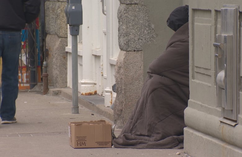 A man sitting outside a building with a blanket and box in downtown St. John's.