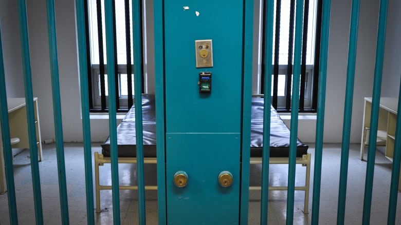 A pair of low beds with thin mattresses can be seen behind bars in two neighbouring jail cells.