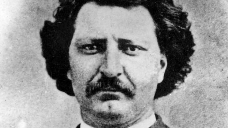 Black and white image of a man's face. He has a moustache and dark wavy hair