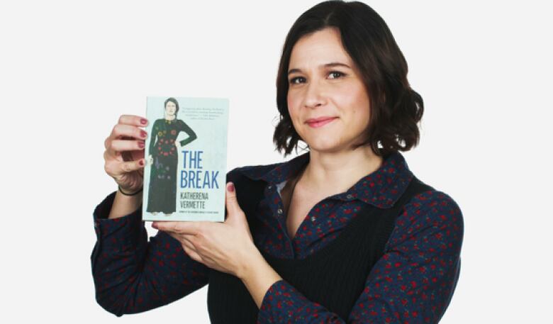 A women with shoulder-length brown hair holding a book up.