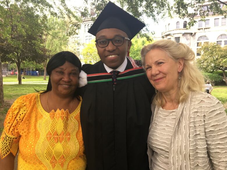 Three people pose together for a photo, the person in the middle wears a graduation gown and cap.