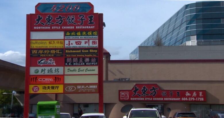 Lots of signs in Chinese on a billboard in front of what looks like a strip mall.