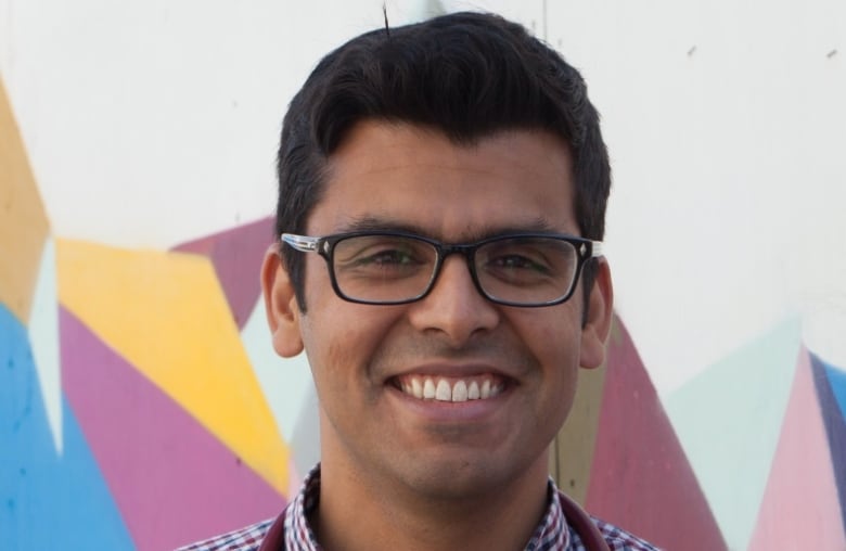 A man with dark hair and glasses smiles.