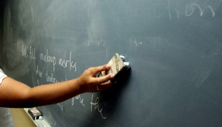 Close up of a teacher's arm using an eraser on a blackboard