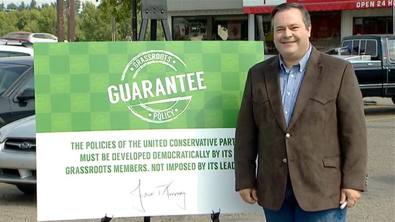 A man smiles while standing next to a political placard.