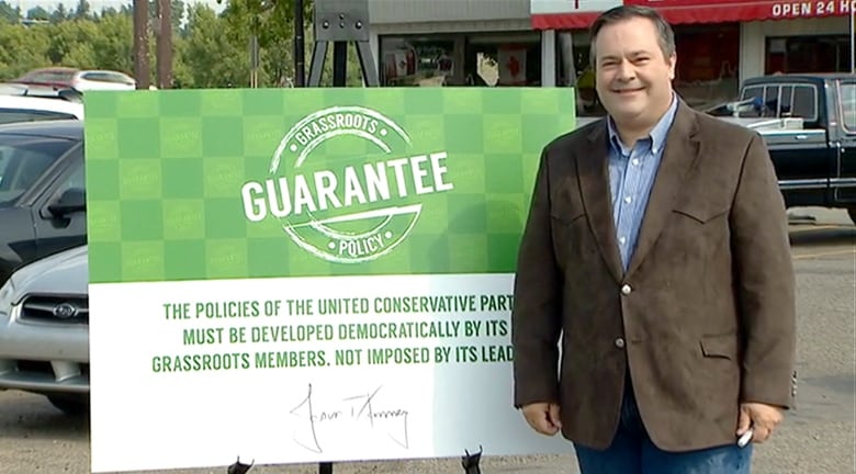 A man smiles while standing next to a political placard.