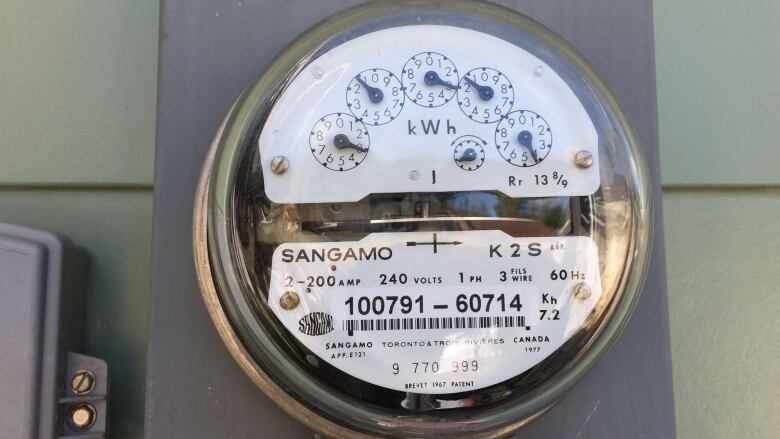 An electric meter is shown close up on the side of a house in daylight.