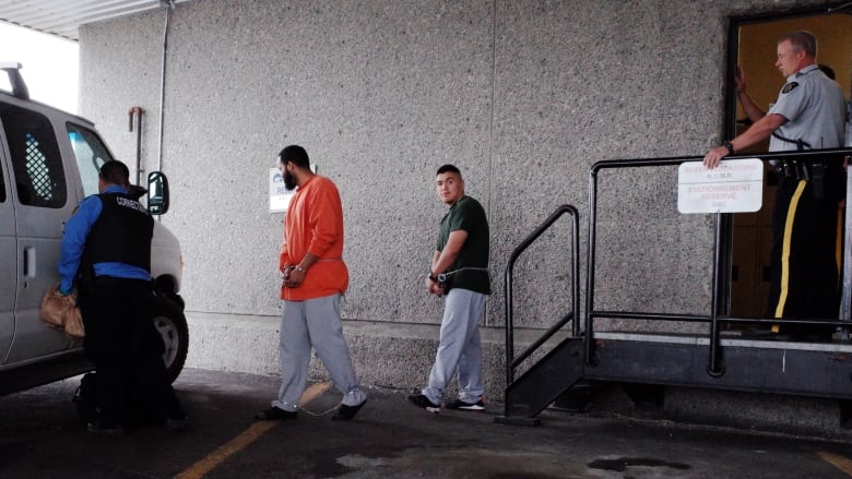 A man walks out of a courthouse in handcuffs with three other people around him 