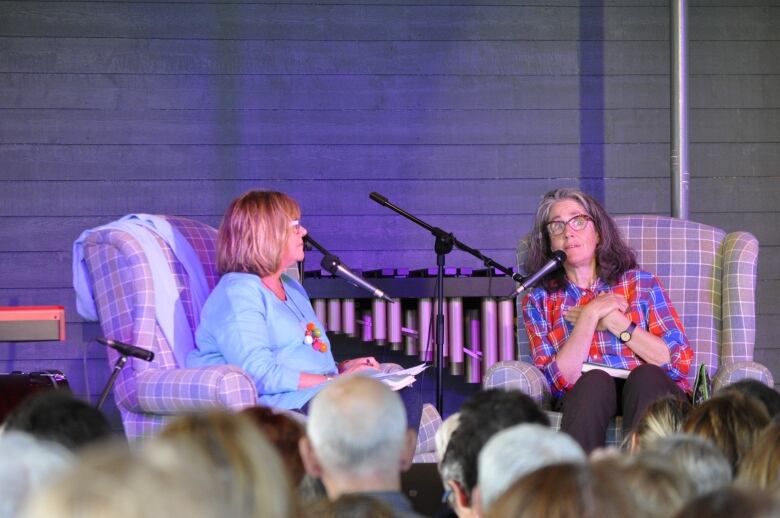 Two women sitting on stage in front of an audience.