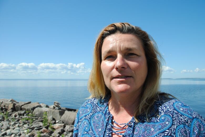 A woman stands in front of a big blue lake on a sunny day 