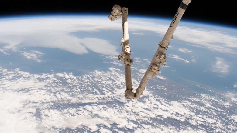 Canada's robotic arm is pictured in space with the Earth in the background.