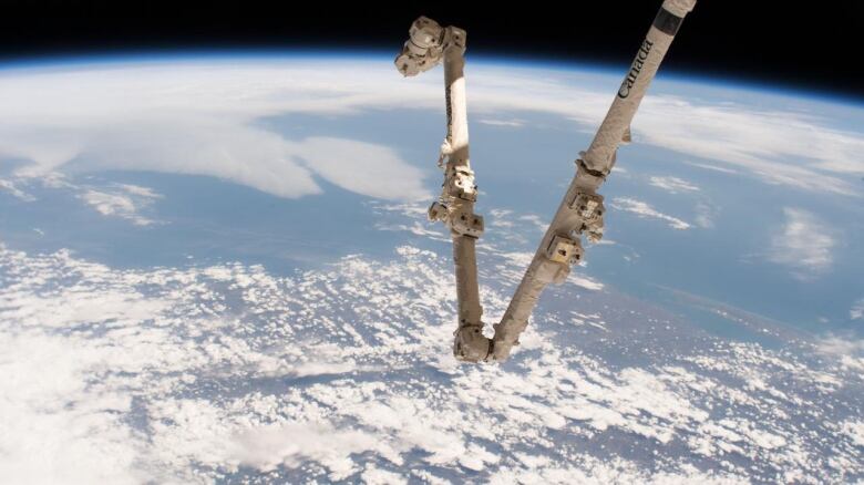 Canada's robotic arm is pictured in space with the Earth in the background.