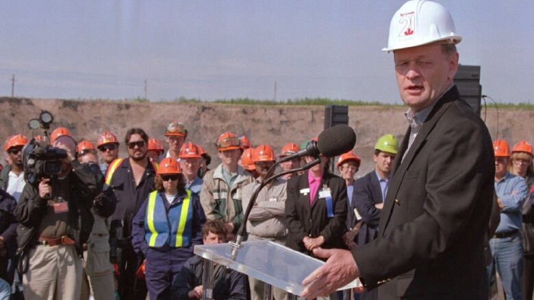 Man at podium in front of oilsands workers