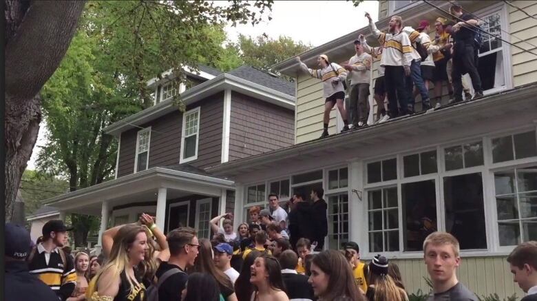 A screengrab of a video of a street party shows many students wearing black, yellow and gold attire, as well as people partying on a roof.