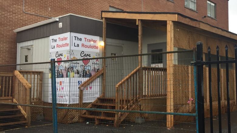 A trailer in a parking lot with wooden ramps and support around it. A sign reads 