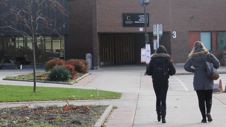 Two people walk away from the camera on a sidewalk on a college campus