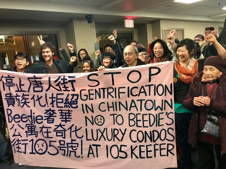 A group of people of diverse ages and races stand clustered around a protest sign that says Stop Gentrification in Chinatown No To Beedie's Luxury Condos at 105 Keefer.