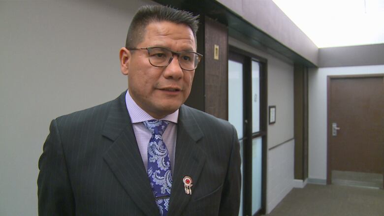 A man in glasses and a suit speaks to a reporter who is off-camera.