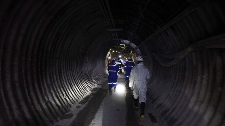 Some people in protective gear walk down a dark tunnel.