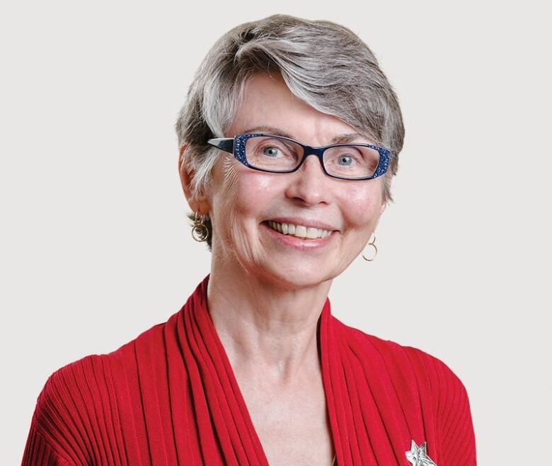 A woman with short grey hair and blue-framed glasses in a red sweater.