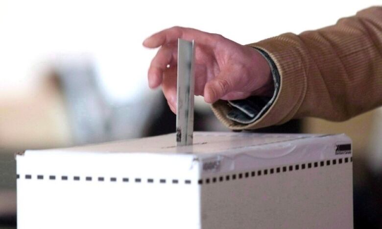 A person puts a ballot into a ballot box.