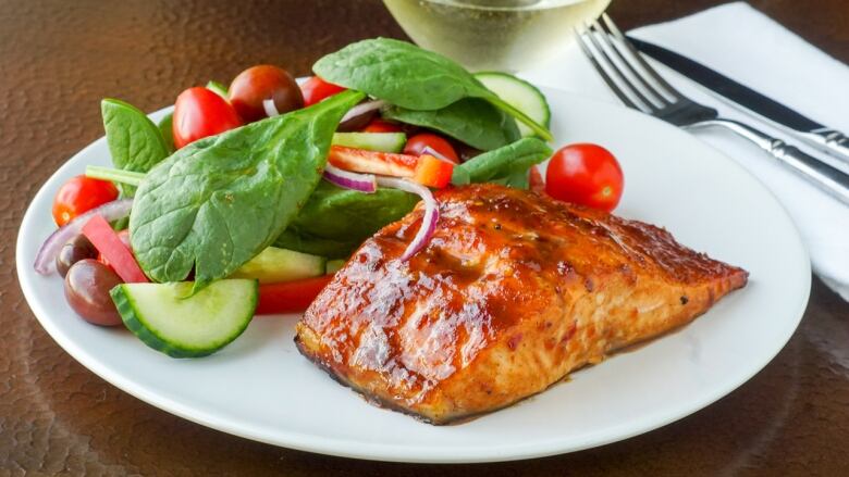 Close up of glazed salmon on a white plate with a salad on the side.