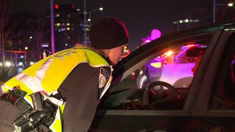 A police officer leans in to speak to a driver at night.