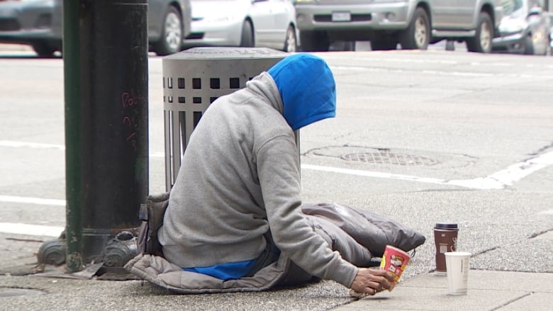 A person experiencing homelessness sitting on the sidewalk with coffee cups. 