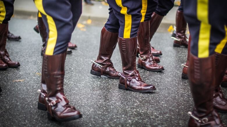 RCMP officers' brown boots are seen marching on a road with the red serge coats also visible