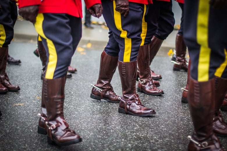 RCMP officers' brown boots are seen marching on a road with the red serge coats also visible