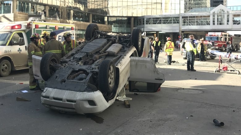 An SUV flipped upside with doors open on a downtown Calgary street.