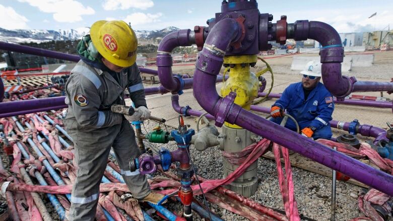 Two workers are seen among a series of pipes. They appear to be fixing some of them.