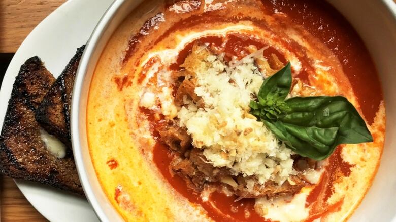 Overhead closeup of a white bowl of tomato soup topped with breadcrumbs, cheese and basil. 