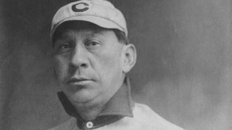 A man sits for a portrait in a baseball uniform.